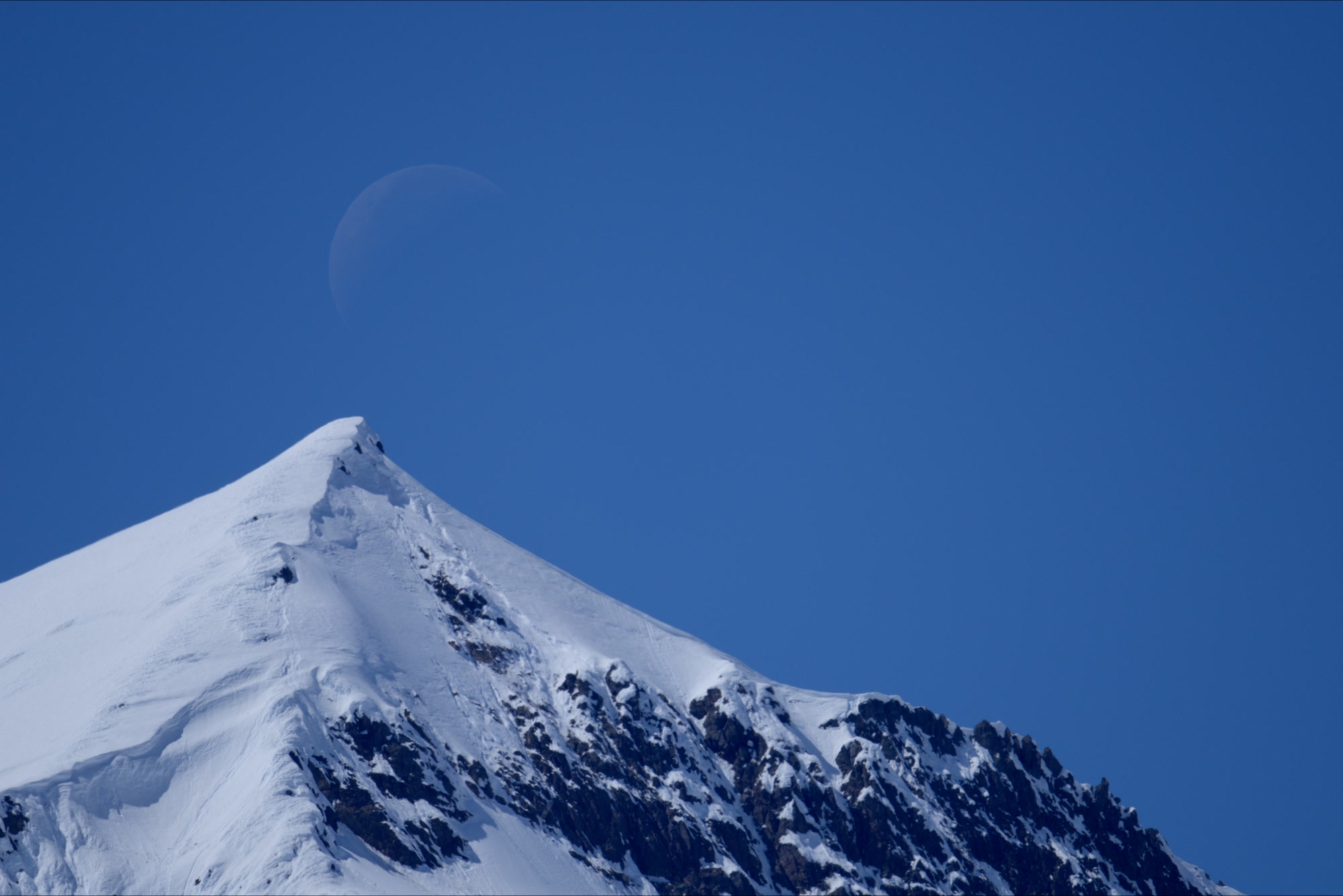 A barely crescent moon rising over the snowy mountains of the Yukon